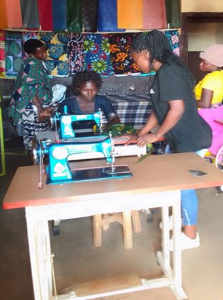 Donatha erhielt ein Startkapital für eine Nähmaschine, jetzt unterrichtet sie andere und verkauft Stoffe.